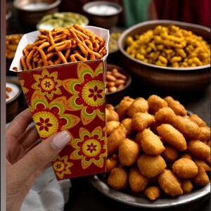 以下が含まれることがあります： 赤と金の模様の紙の円錐形に、カリカリの揚げた軽食が詰まっている。円錐形は手で持たれている。背景には、小さな丸い金色をした揚げた軽食など、他の揚げた軽食が入ったボウルがある。