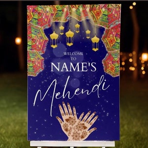 May include: A blue and gold welcome sign for a Mehndi party. The sign features a decorative border with hanging lanterns and a pair of hands with henna designs. The text on the sign reads "Welcome to NAME'S Mehndi".