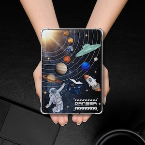 以下が含まれることがあります： 鮮やかな宇宙をテーマにしたデザインの透明な携帯電話ケース。デザインには、惑星、ロケット、宇宙飛行士、UFOが、暗い青色の星空の背景に描かれています。「DANGER CLEAR THIS AREA」というテキストも表示されています。