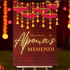 Puede incluir: Un cartel de bienvenida rojo y dorado con el texto "Bienvenido a Apana's Mehendi" sobre un fondo rojo oscuro con un diseño estampado. El cartel está decorado con campanas doradas colgantes y acentos florales rosas y verdes.