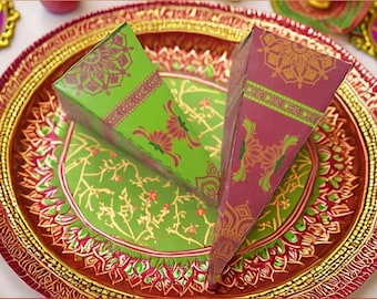 Puede incluir: Dos conos de papel decorativos con intrincados diseños florales y geométricos. Los conos son verdes y morados con detalles dorados y están sobre un plato rojo y dorado.