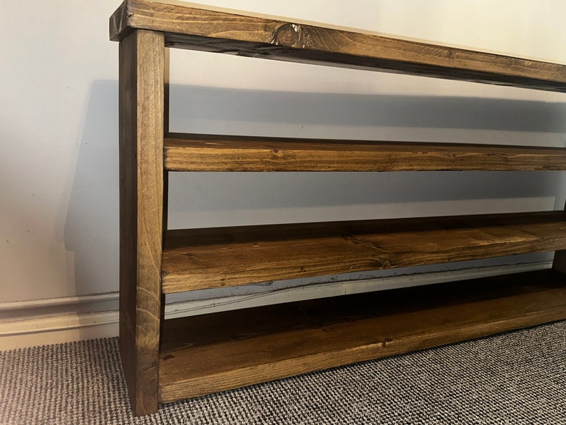 May include: A handcrafted wooden shelf with a rich, dark brown stain. The shelf has four horizontal levels supported by vertical side pieces. The wood grain is visible, adding to the rustic aesthetic. Perfect for storage or display.