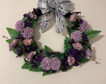 May include: A purple and green floral wreath with a white bow featuring a lavender print. The bow has a price tag attached to it.
