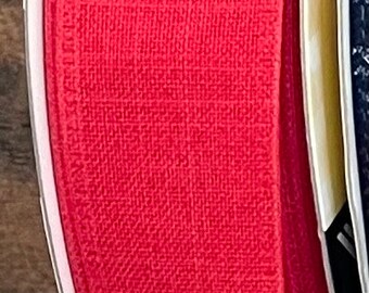 May include: Close-up of a roll of red fabric ribbon. The ribbon has a textured weave and is wrapped around a white core. The edge of a second roll of ribbon is visible.