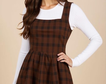 May include: A brown and black plaid pinafore dress with a white long-sleeved shirt underneath. The dress has a square neckline and a flared skirt.