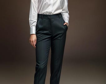 May include: A woman wearing a white button-down shirt and black tailored pants. She is standing with one hand in her pocket and the other by her side.