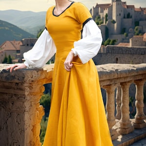 May include: A woman in a yellow medieval dress with white puffed sleeves stands on a stone balcony overlooking a medieval castle. The dress has a black trim around the neckline and hem.