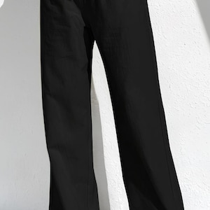 May include: Black wide-leg trousers with an elasticated waistband. The trousers are made of a lightweight fabric and have a relaxed fit. The trousers are paired with white trainers.
