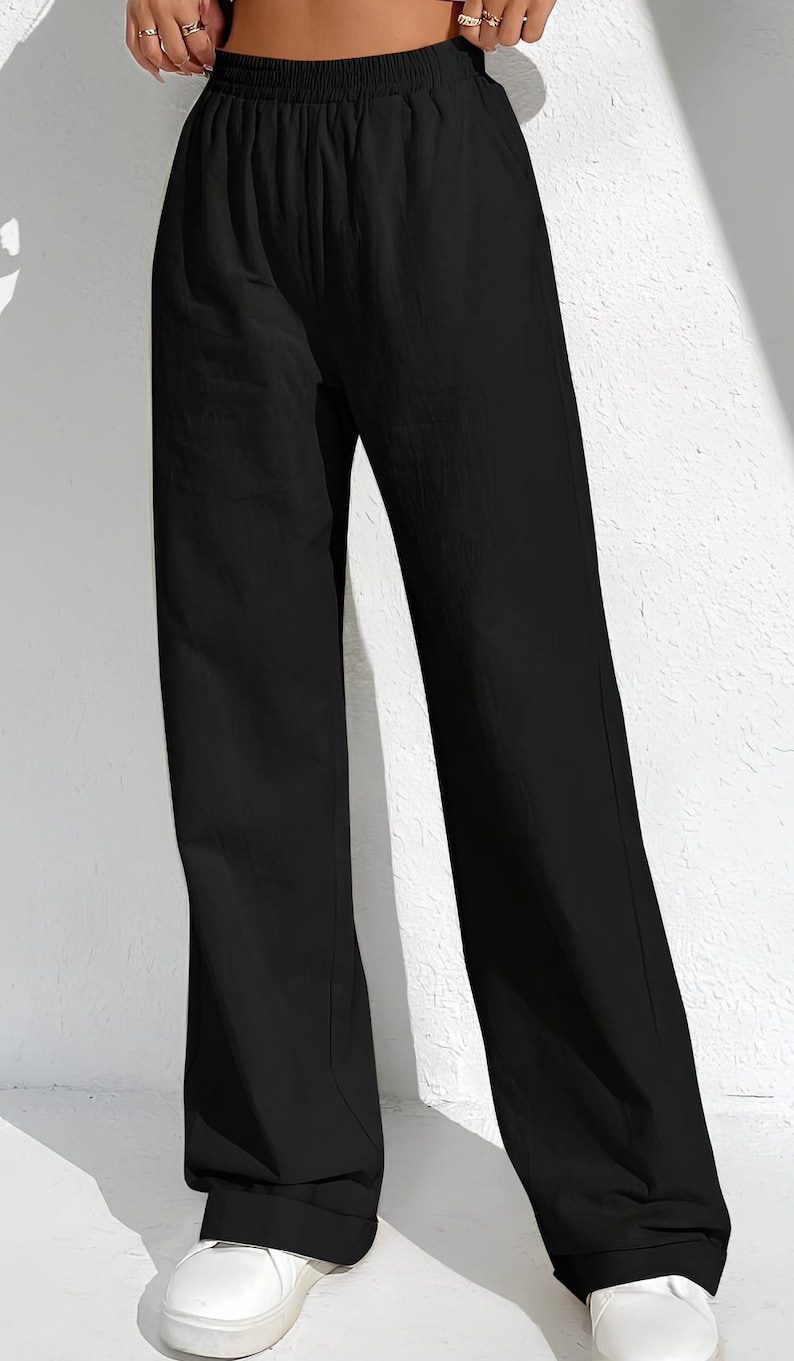 May include: Black wide-leg trousers with an elasticated waistband. The trousers are made of a lightweight fabric and have a relaxed fit. The trousers are paired with white trainers.