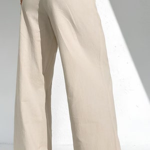 May include: Beige wide-leg trousers with an elasticated waistband. The trousers are made of a lightweight fabric and have a relaxed fit. The bottom of the trousers are cuffed. The trousers are paired with white trainers.
