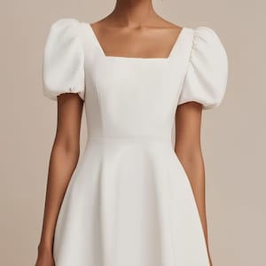 May include: A white, simple wedding dress with a square neckline and puffed sleeves. The dress has a fitted bodice and a flowing skirt.