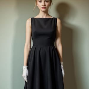 Pu&ograve; includere: Una donna indossa un abito nero senza maniche con scollo a barca e gonna ampia. Indossa guanti bianchi.