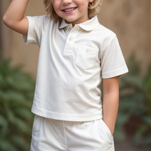 Puede incluir: Un ni&ntilde;o peque&ntilde;o con una camisa polo blanca de manga corta y pantalones cortos blancos a juego. El ni&ntilde;o sonr&iacute;e y tiene el pelo rubio.