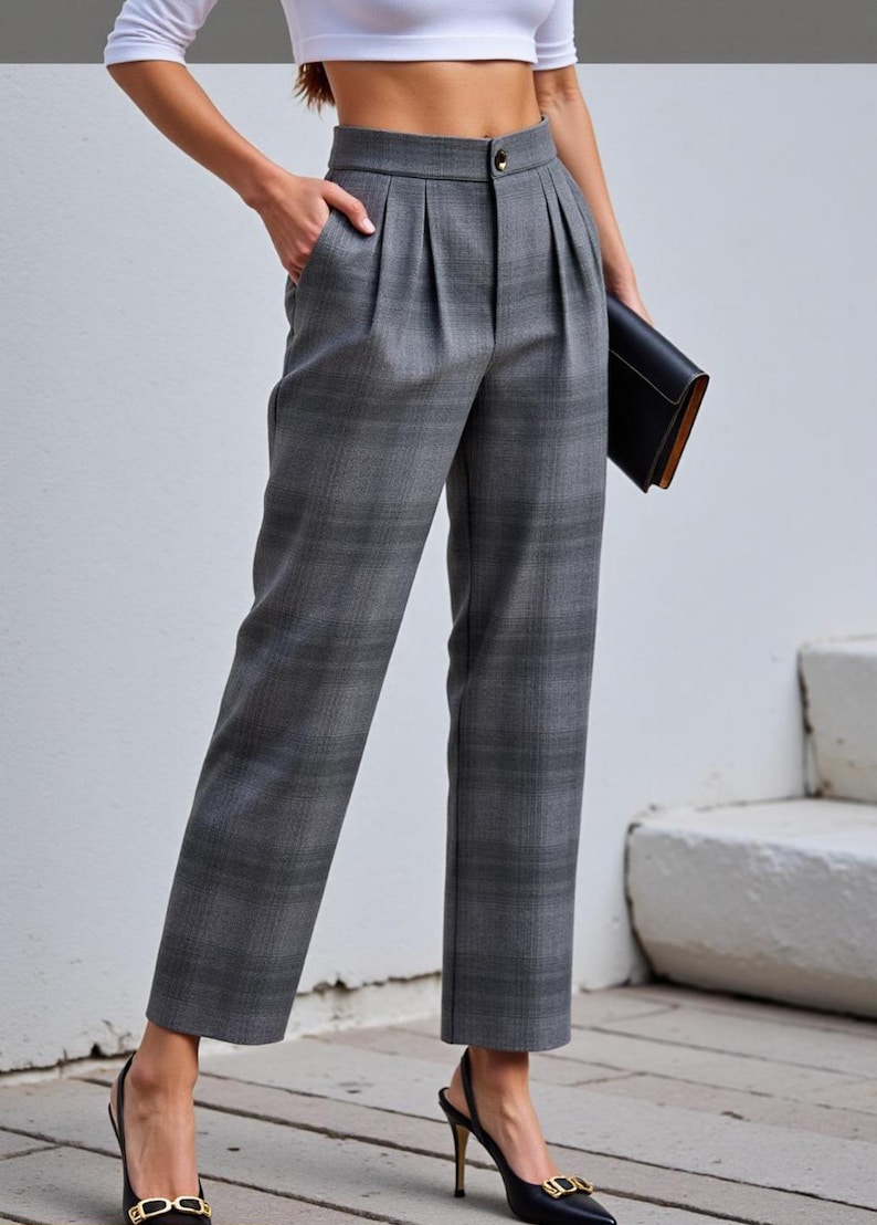 Puede incluir: Pantalones grises a cuadros con cintura alta y pliegues. Los pantalones tienen cierre de bot&oacute;n y bolsillos. La modelo lleva tacones negros y sostiene un clutch negro. Los pantalones son de estilo cl&aacute;sico.