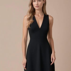 Puede incluir: Un vestido negro sin mangas, corto, con un escote en V profundo. El vestido tiene un corpiño ajustado y una falda acampanada.