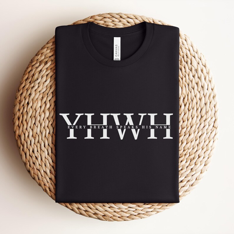 K&ouml;nnte beinhalten: Schwarzes T-Shirt mit dem wei&szlig;en Text "YHWH EVERY BREATH SPEAKS HIS NAME". Das Shirt ist gefaltet und auf einer gewebten, kreisf&ouml;rmigen Oberfl&auml;che platziert. Das Shirt hat ein Etikett mit der Aufschrift "Canvas".