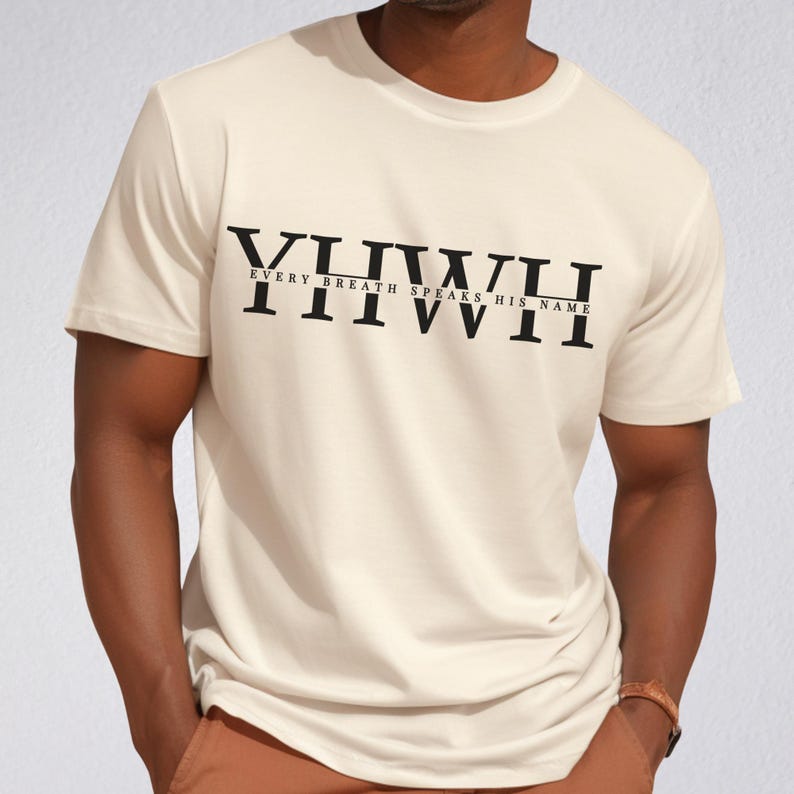 K&ouml;nnte beinhalten: Cremefarbenes T-Shirt mit dem Text "YIIWII EVERY BREATH SPEAKS HIS NAME" in Schwarz. Das Shirt hat kurze &Auml;rmel und einen Rundhalsausschnitt. Die Person tr&auml;gt eine Uhr.