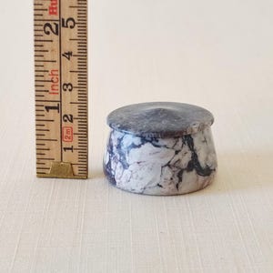 May include: A small, round marble container with a lid. The container is approximately 5 cm in diameter and 5 cm tall. The marble has a white and gray pattern. The lid is a solid gray colour.