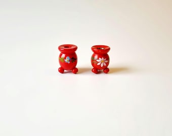 May include: Two small red wooden candle holders with painted floral designs. The candle holders have three legs each.