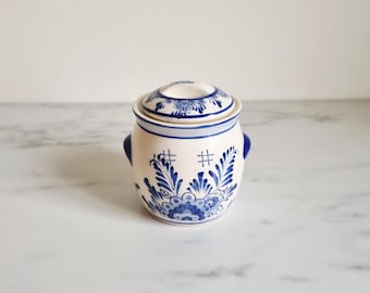 Peut inclure: Petit pot en céramique avec couvercle, orné d'un motif floral bleu et blanc. Le pot a deux petites poignées et est décoré de motifs complexes. Le couvercle présente également un motif floral. Le pot est probablement destiné au stockage.
