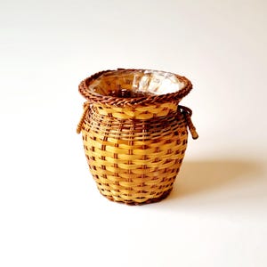 May include: A woven wicker basket with a brown and tan pattern. The basket has two small handles on the sides and is perfect for holding small items.