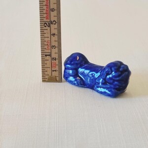 May include: A cobalt blue ceramic figurine, approximately 2 inches long, with a glossy finish. The figurine has a rounded shape with textured details. A wooden ruler is next to the figurine.