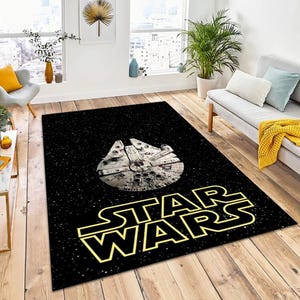 May include: Black rectangular Star Wars area rug featuring the Millennium Falcon spaceship design. The Star Wars logo is in yellow. The rug is on a hardwood floor in a room with natural light.