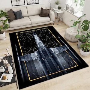 May include: Black rectangular area rug featuring a detailed illustration of a spaceship in flight against a starry background. The spaceship is rendered in shades of gray and silver, framed by a gold border. The rug is designed for home decor.