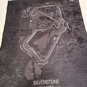 May include: A black and white map of the Silverstone racetrack in Great Britain. The map shows the layout of the track and surrounding area. The text "SILVERSTONE" and "GREAT BRITAIN" is printed in white at the bottom of the map. The coordinates "52&deg;04'26.0"N 1&deg;00'52.8"W" are printed below the text.