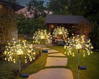 May include: Four solar powered firework lights illuminate a pathway in a garden. The lights are made of thin metal wires with small white LED lights that create a firework effect. The lights are on stakes that are inserted into the ground.