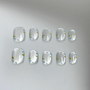 May include: Set of ten white square-shaped false nails with a floral design. The nails have a light blue and green floral pattern.