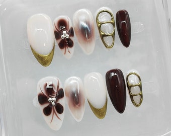 May include: A set of ten false nails with a variety of designs. The nails are in a clear plastic case. Some nails have a floral design, some have a gold accent, and some are a solid color.
