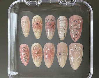 May include: A clear plastic case containing ten false fingernails with various designs. The designs include butterflies, flowers, hearts, and rhinestones.