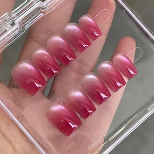 Könnte beinhalten: Ein Set aus zehn künstlichen Nägeln mit Farbverlauf. Die Nägel gehen von einem hellen Rosa an der Basis zu einem tiefen Rot an den Spitzen über. Sie sind glänzend und scheinen sich in einer transparenten Kunststoffhülle zu befinden.
