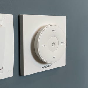 May include: A white wall-mounted light switch and a circular control panel. The control panel has a central power button and labels for dimming and color temperature adjustment. The brand name "MiBoxer" is printed on the panel.