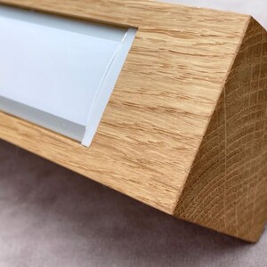 May include: A rectangular wooden object with a light-colored, possibly frosted, glass insert. The wood has a natural grain and a warm, light brown color. The object has a geometric, angled design.