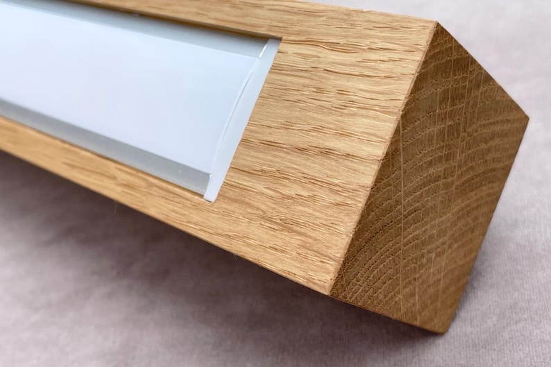 May include: A rectangular wooden object with a light-colored, possibly frosted, glass insert. The wood has a natural grain and a warm, light brown color. The object has a geometric, angled design.