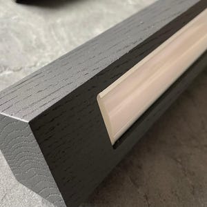 May include: Close-up of a gray wooden beam with a recessed, illuminated light strip. The wood grain is visible, and the light strip emits a soft, warm glow. The beam has a modern, minimalist design, suitable for interior design.
