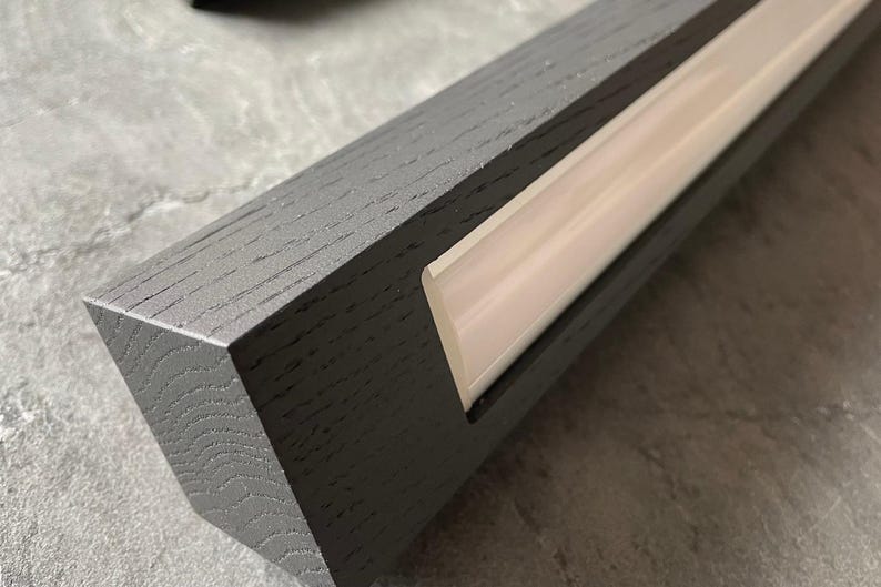May include: Close-up of a gray wooden beam with a recessed, illuminated light strip. The wood grain is visible, and the light strip emits a soft, warm glow. The beam has a modern, minimalist design, suitable for interior design.