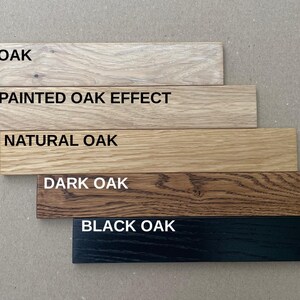 May include: Five wooden planks showcasing different oak finishes: White Oak, Unpainted Oak Effect, Natural Oak, Dark Oak, and Black Oak. Each plank has the finish name printed in white.