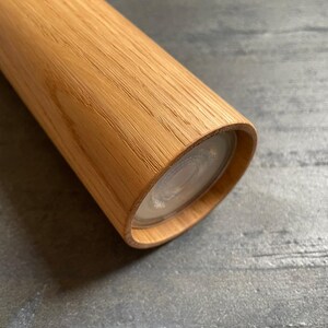 May include: Close-up of a wooden cylindrical object with a light-colored, transparent end. The wood grain is visible, and the object appears to be a kitchen or home decor item. The wood has a warm, natural tone.