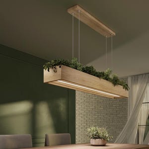 Może przedstawiać: Prostokątna drewniana lampa wisząca z wbudowaną skrzynką na rośliny wypełnioną zielenią. Lampa ma liniowe źródło światła LED i jest zawieszona pod sufitem za pomocą cienkich przewodów. Oprawa jest zawieszona nad drewnianym stołem.