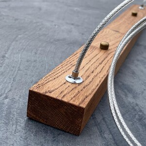 May include: Close-up of a rectangular, light brown wooden block with two silver cables and small brass and silver hardware. The wood grain is visible. The cables are braided and appear to be for a light fixture.