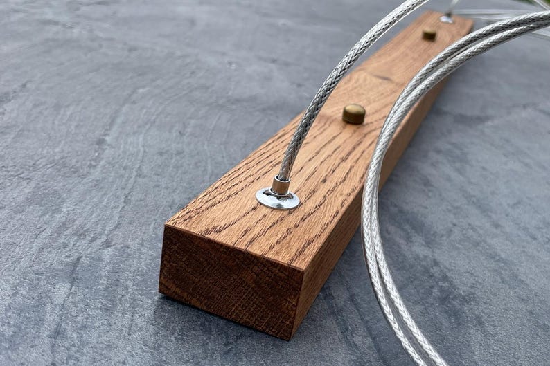 May include: Close-up of a rectangular, light brown wooden block with two silver cables and small brass and silver hardware. The wood grain is visible. The cables are braided and appear to be for a light fixture.