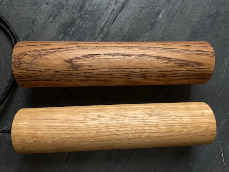 May include: Two cylindrical wooden objects with black cords attached. One is a light brown color, and the other is a darker brown with visible wood grain. The objects are likely handles or decorative elements.