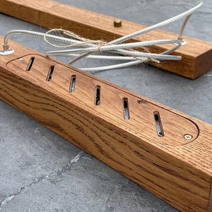 May include: Two rectangular wooden light fixtures with a natural wood grain finish. Each fixture has a series of slotted openings and a recessed area for wiring. White braided cords and a brass-colored screw are visible.
