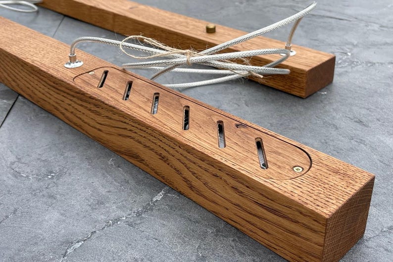 May include: Two rectangular wooden light fixtures with a natural wood grain finish. Each fixture has a series of slotted openings and a recessed area for wiring. White braided cords and a brass-colored screw are visible.