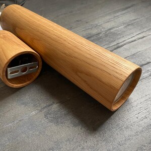 May include: A wooden cylindrical pendant light fixture with a natural wood grain finish. The fixture is composed of two parts: a long, cylindrical body and a smaller, circular base. The base has a metal mounting bracket. The light fixture is designed for ceiling installation.