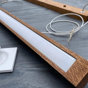 May include: A wooden LED light fixture with a white light strip, a white remote control, and a white base with the text "HIBOXER". The fixture has a natural wood grain finish and a white power cord.