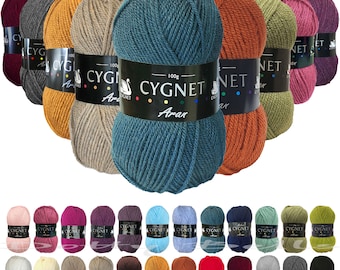Pode incluir: Conjunto de 24 novelos de lã em várias cores, incluindo vermelho, laranja, amarelo, verde, azul, roxo, marrom e cinza. Cada novelo é etiquetado com "CYGNET Aran" e tem um logotipo de cisne branco.
